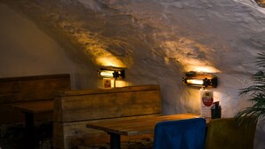 Un interior con pared de piedra rústica, bancos de madera y lámparas colgantes.