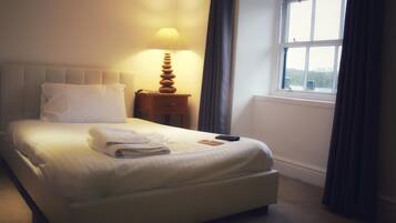 A neatly made bed with a folded towel, a bedside lamp, and a remote control on the nightstand.