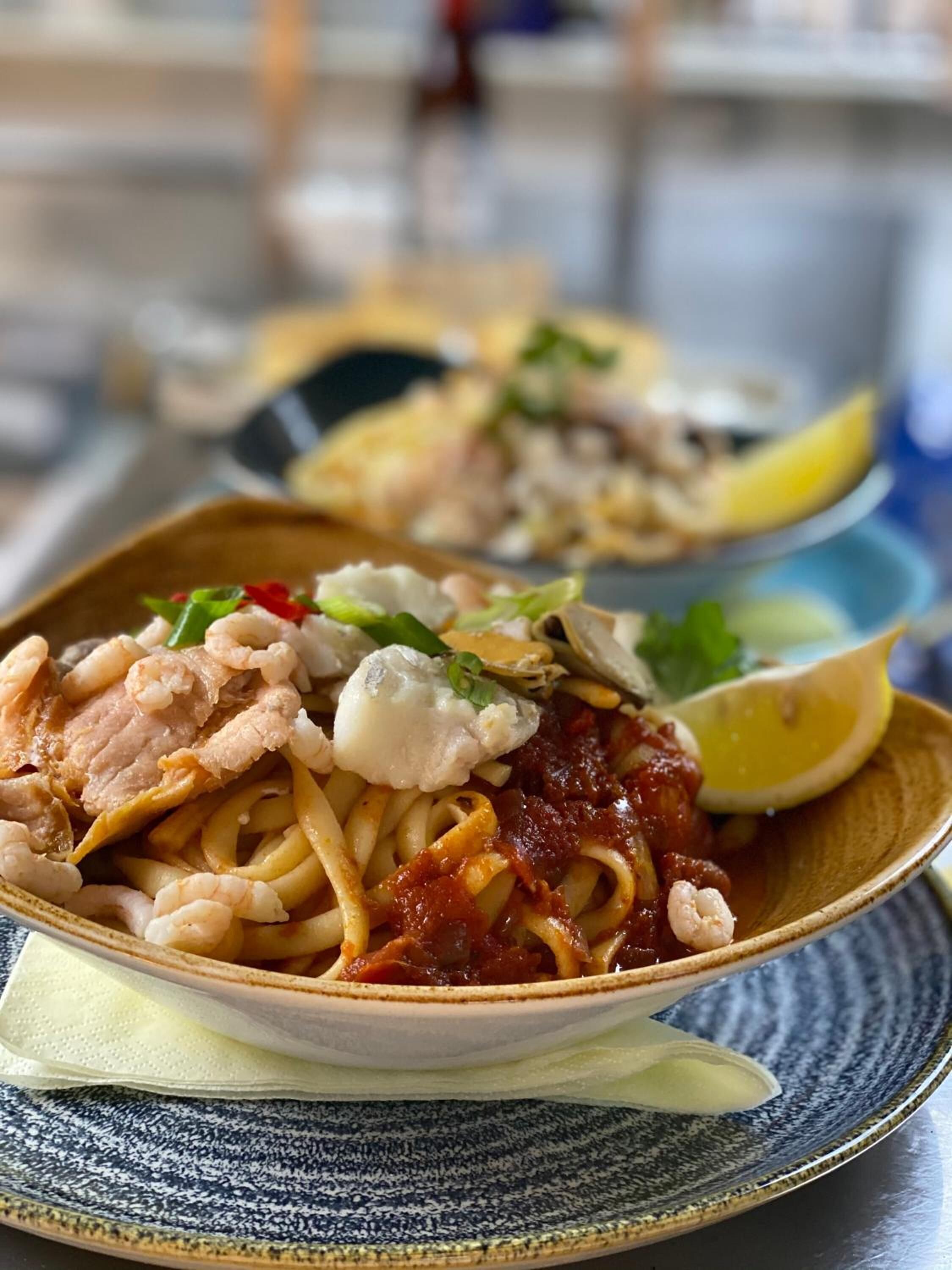 Eine Schüssel Pasta mit Garnelen und einem Zitronenspalte daneben.