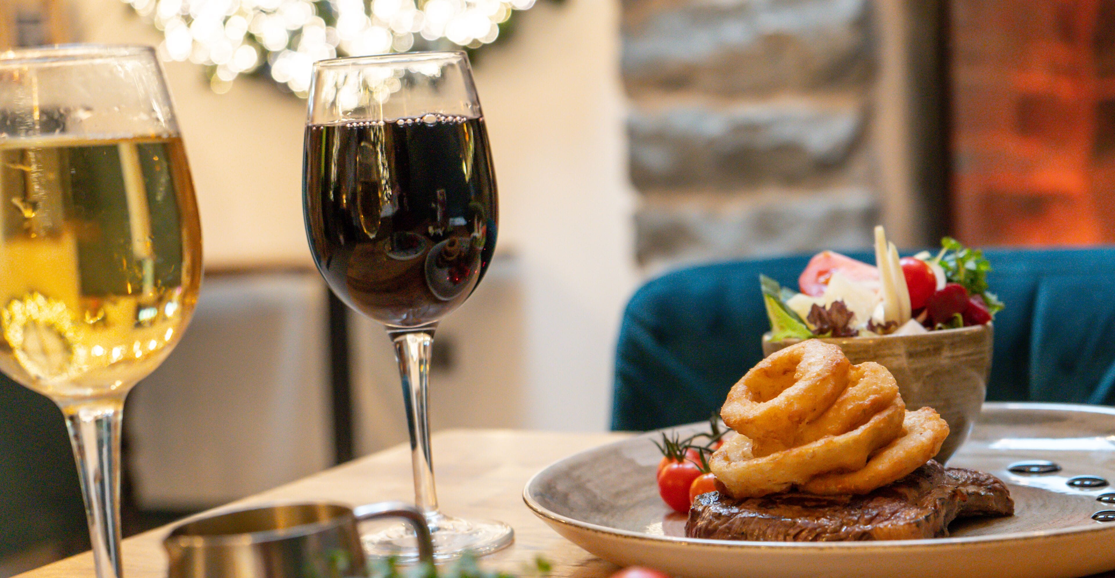 A dining table with a plate of food, a glass of white wine, and a glass of red wine.