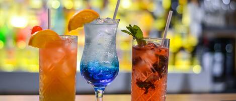 Three different drinks on a bar counter with a blurred background of shelves with bottles.