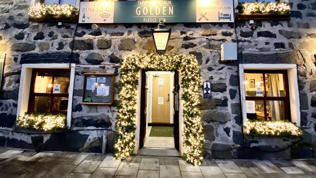Un edificio de piedra con un letrero que dice "GOLDEN FLEECE INN" y una decoración de árbol de Navidad.