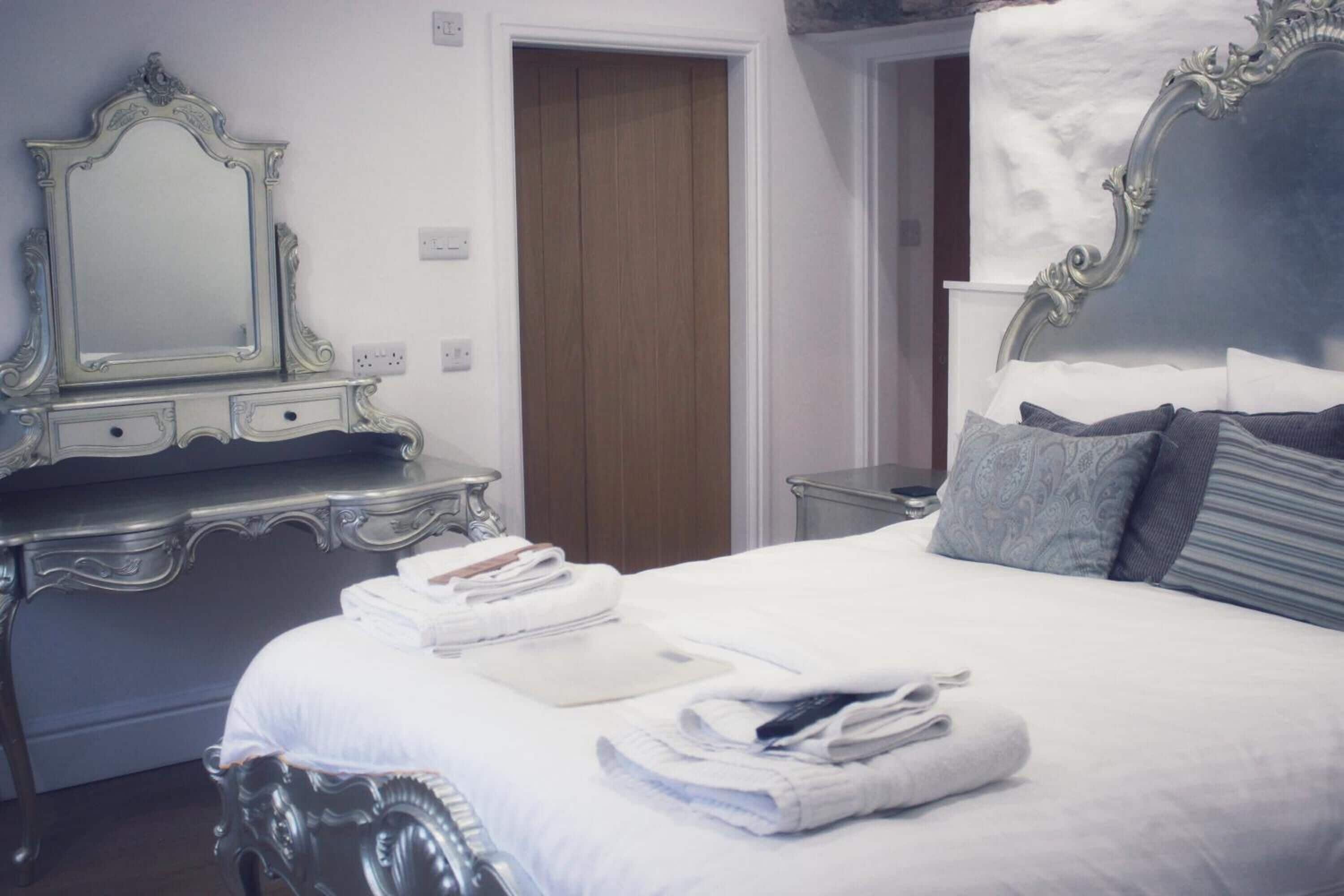 A neatly made bed with folded towels, a dresser with a mirror, and a door in the background.