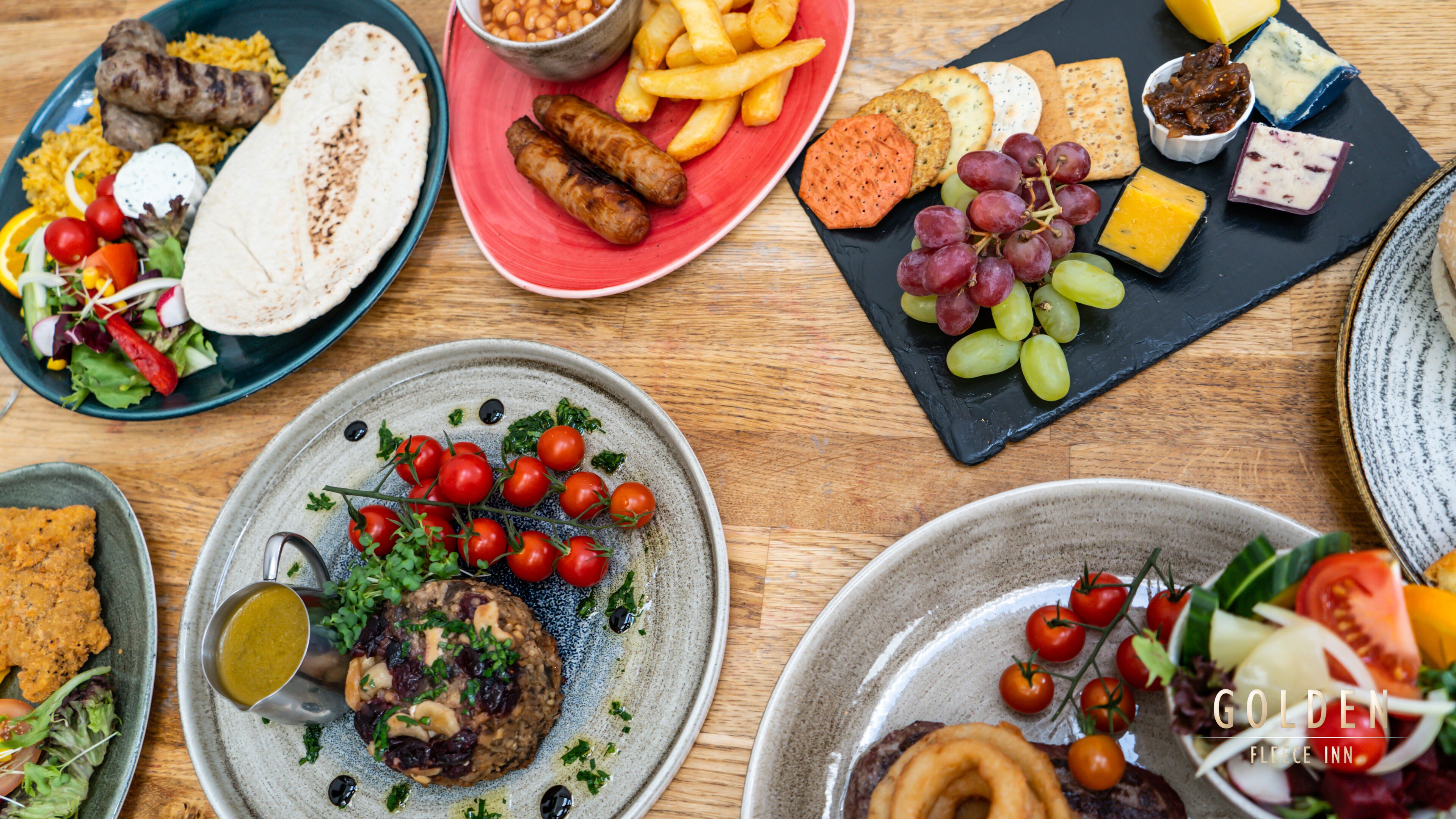 Diverse gerechten op een houten tafel, waaronder vlees, kaas en groenten.
