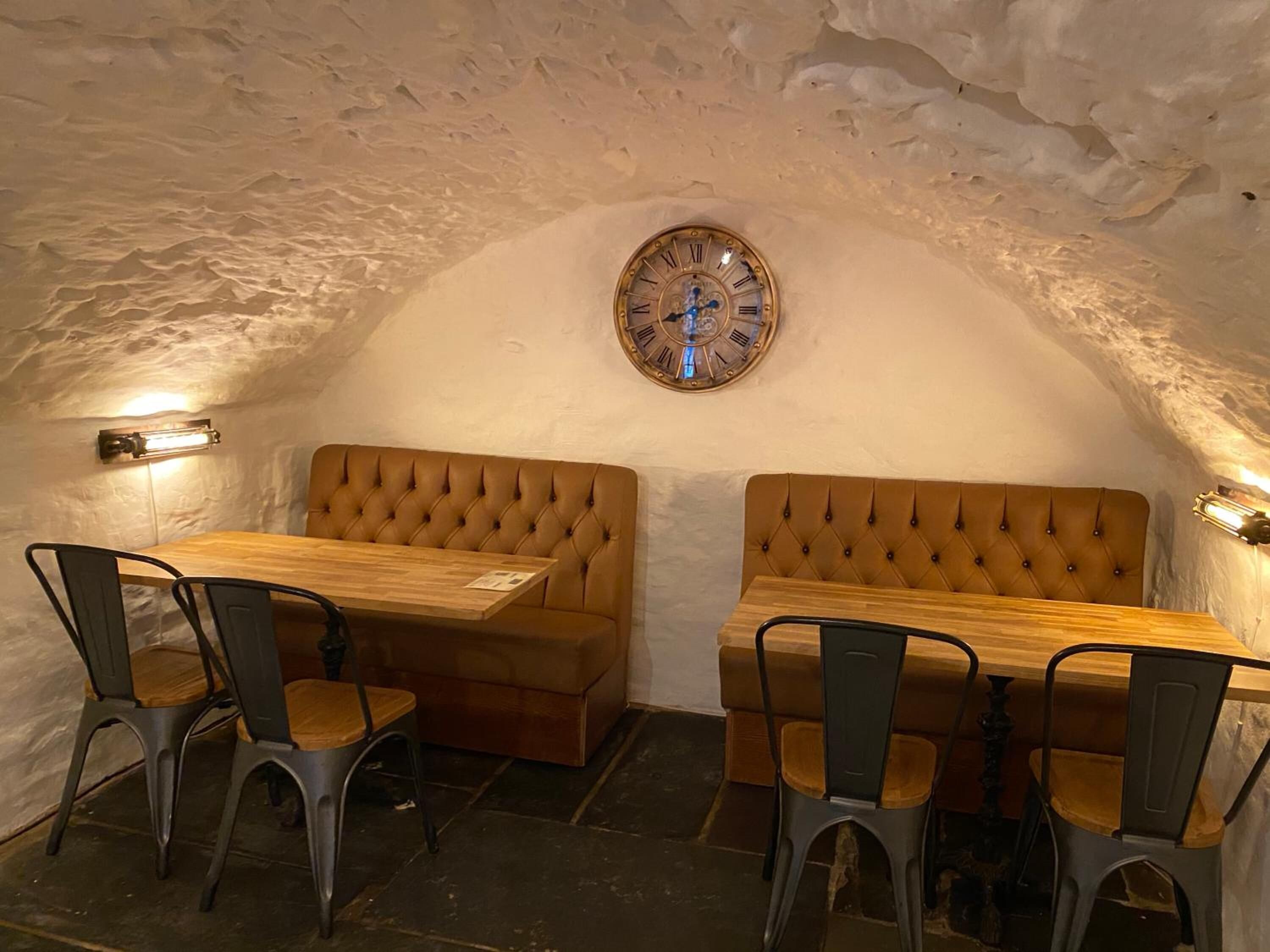 Um interior acolhedor com uma mesa de madeira e dois bancos estofados, um relógio na parede e duas luminárias de parede.
