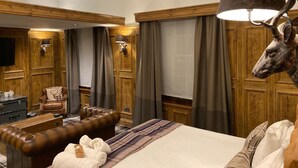 Habitación de hotel con una cama grande, un sofá de cuero, un cabecero de madera, una cabeza de venado montada y un televisor.