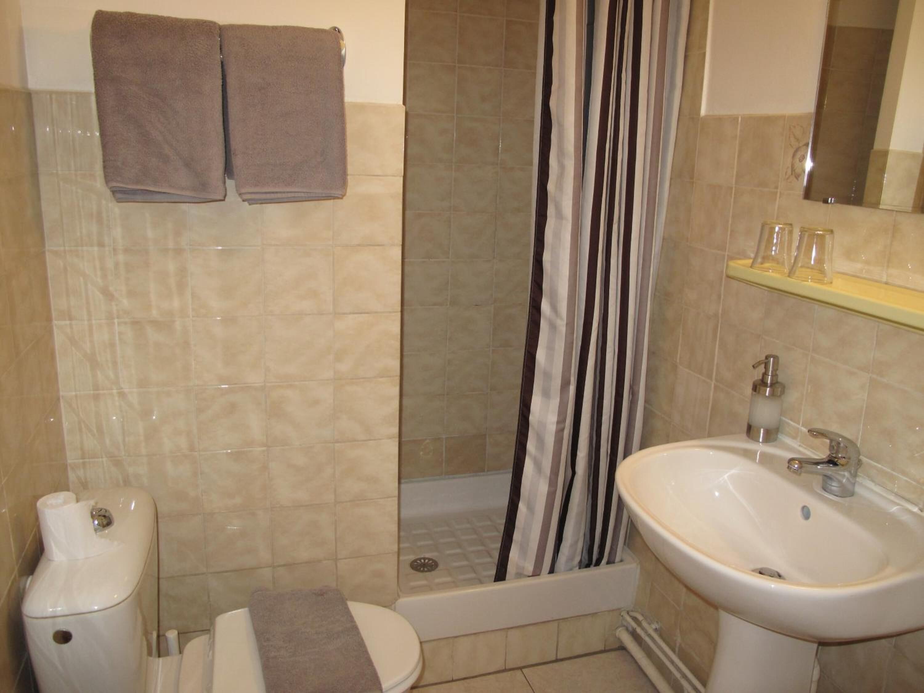 A bathroom with a toilet, a sink, and a shower with a striped curtain. There are two towels hanging on the wall.