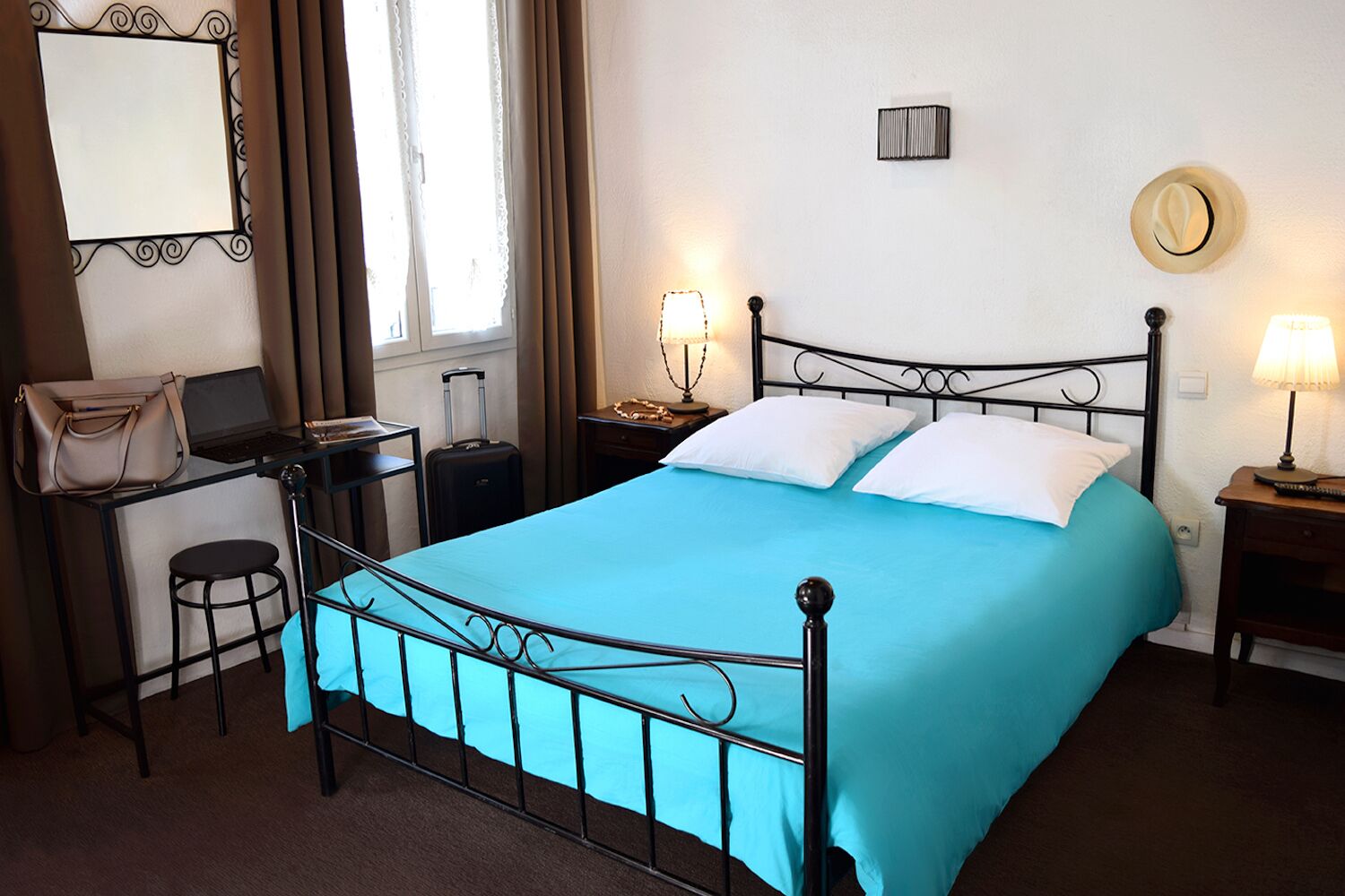 A hotel room with a bed, a desk with a laptop, a suitcase, and a handbag.