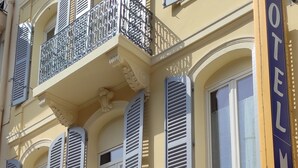 Um hotel com varanda, janelas amplas e uma placa indicando o nome do hotel.