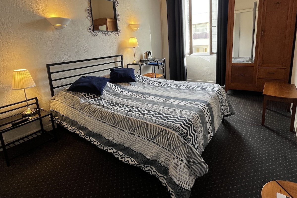A bedroom with a bed, bedside lamps, a desk, a chair, a wardrobe, and a ceiling fan.