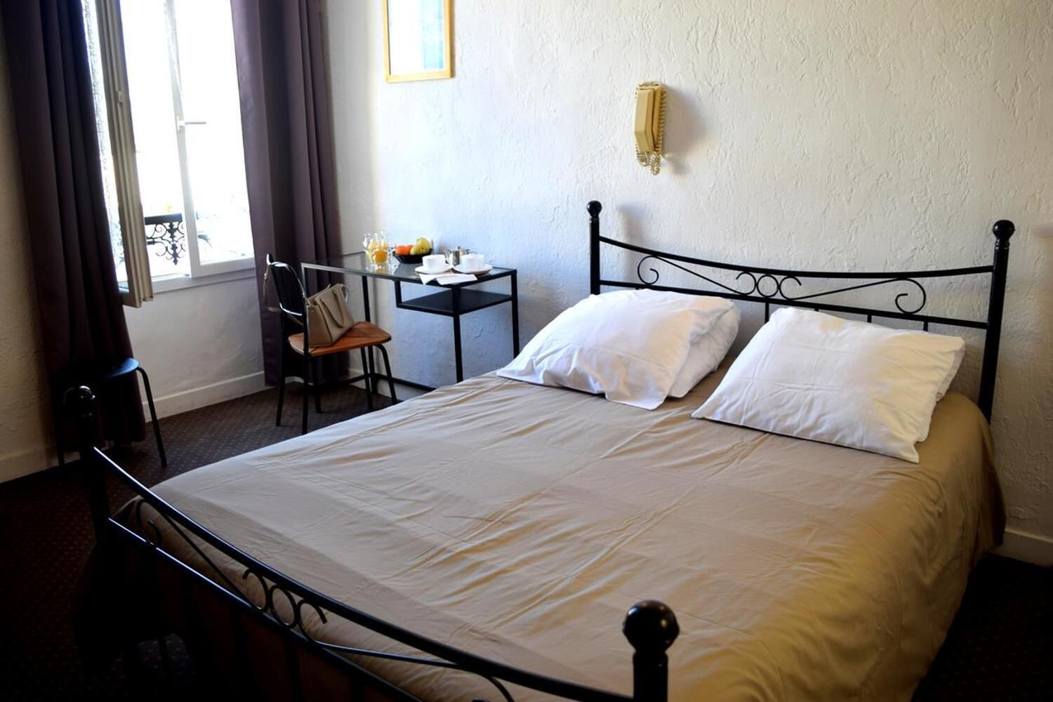 A neatly made bed with white linens, a small table with a chair, and a window with curtains.