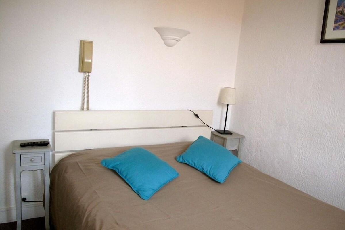 Una habitación de hotel con cama, dos almohadas, una lámpara de noche, teléfono y una mesita.