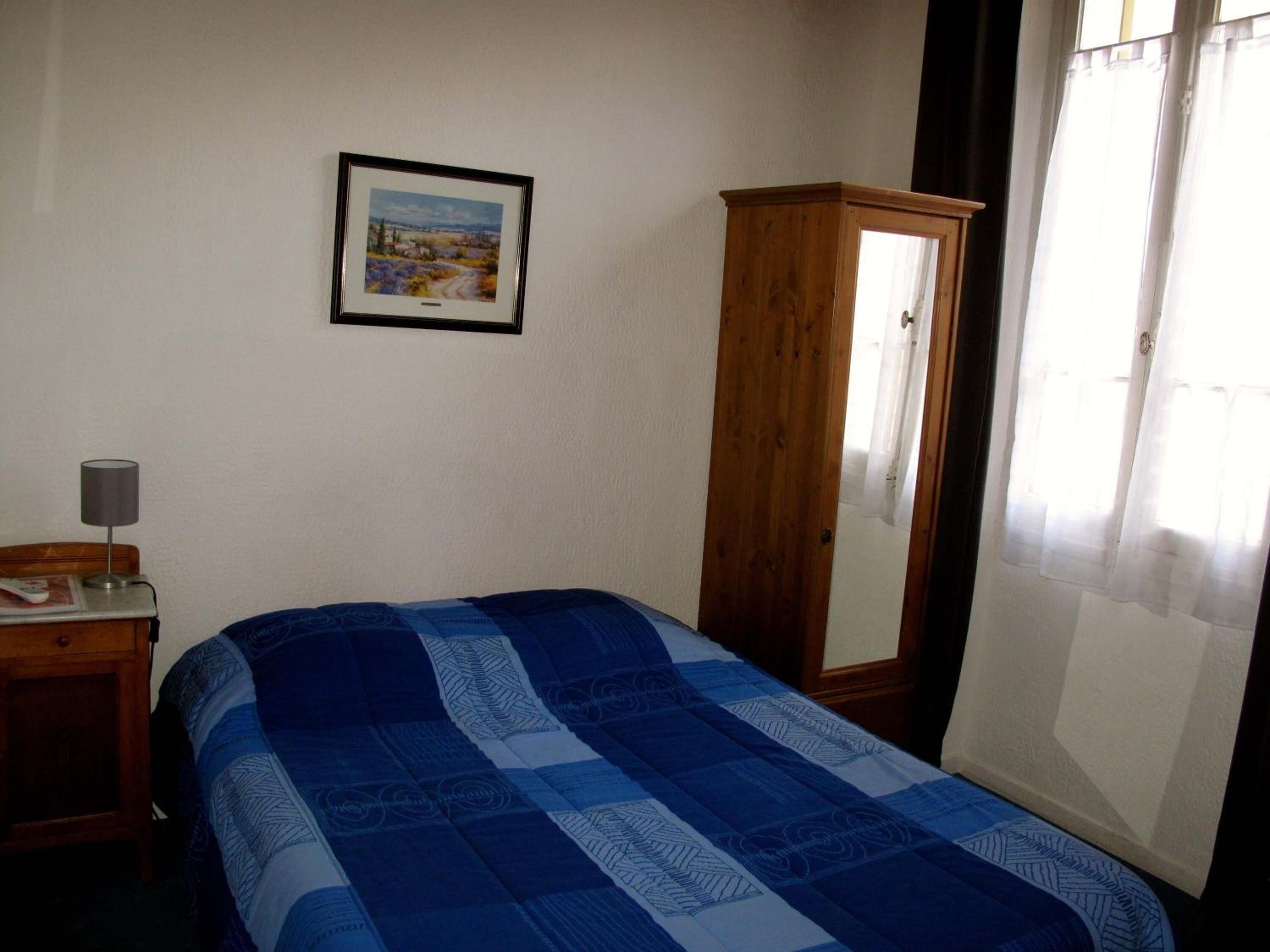 Un dormitorio con cama, un armario de madera, una mesita de noche con lámpara y un cuadro enmarcado en la pared.