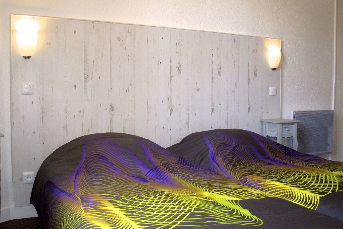 A hotel room with a wooden headboard, two bedside tables, and a wall-mounted light fixture.