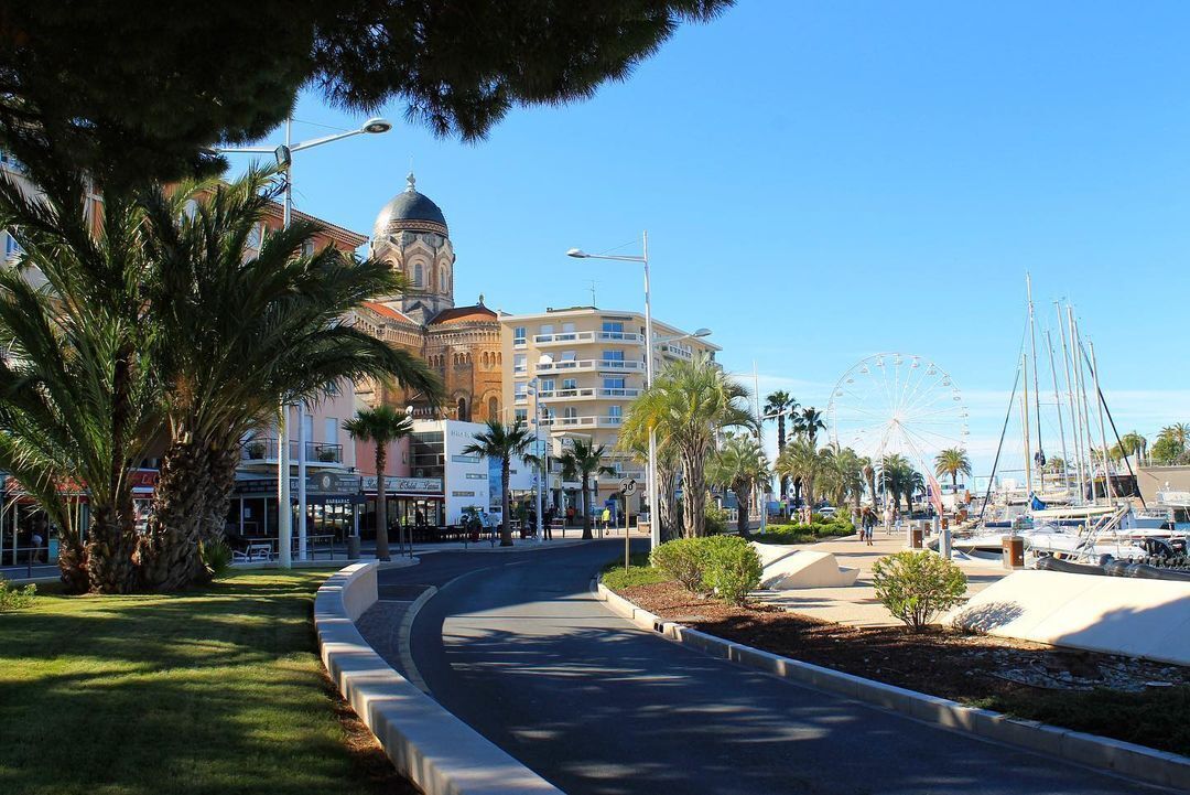 Una passeggiata costiera con una strada curva, palme, un grande edificio con una cupola e una ruota panoramica sullo sfondo.