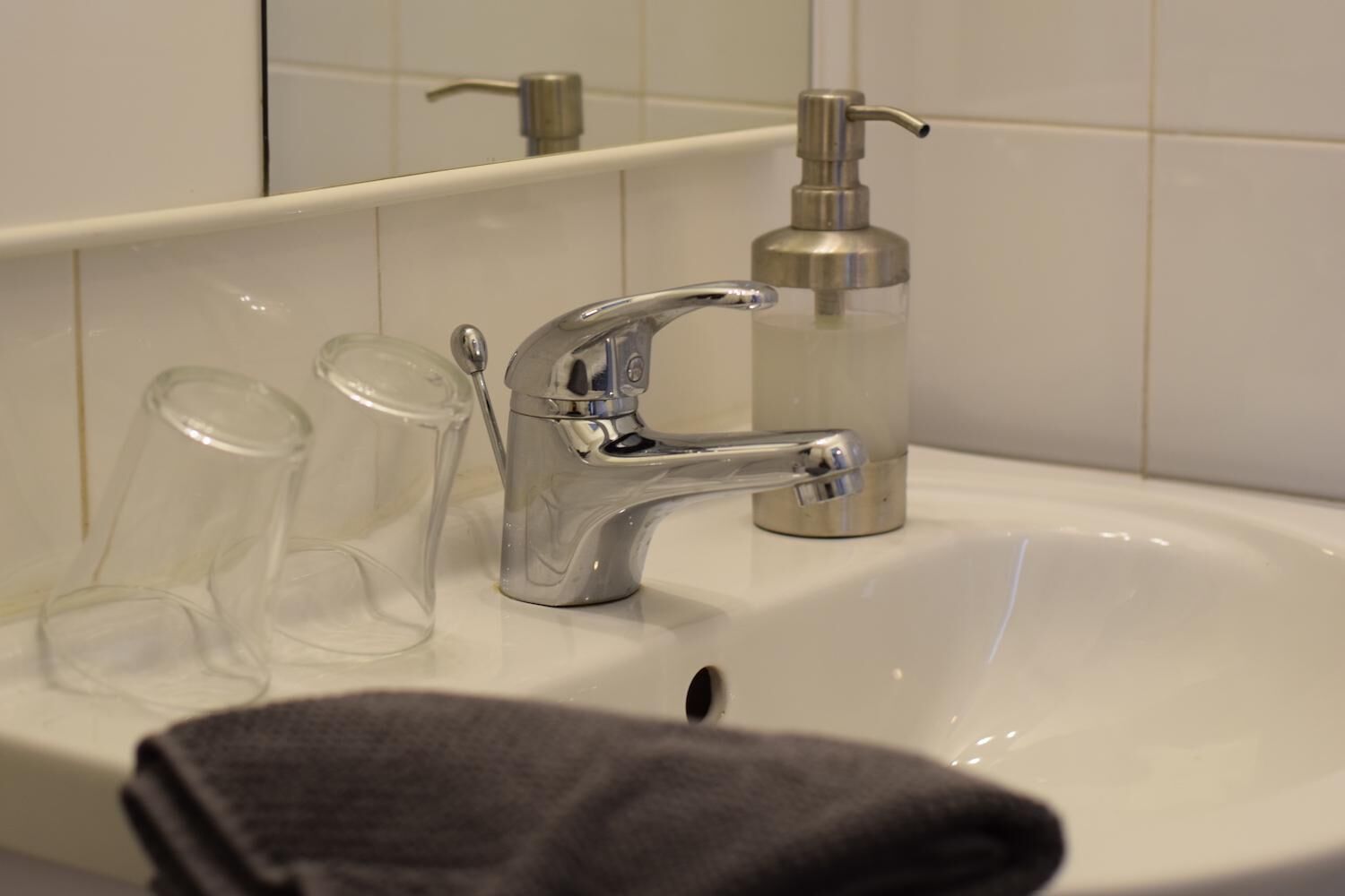 A bathroom sink with a chrome faucet, a soap dispenser, and two clear glasses.