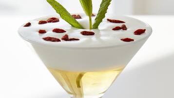 Una copa de martini con una capa blanca y cremosa, adornada con hojas de menta y bayas rojas, sobre una superficie blanca.