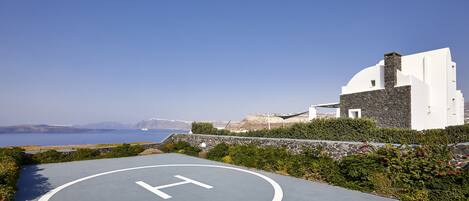 A building with a helipad marked with a large 'H' on the ground, surrounded by greenery and overlooking a scenic coastline.