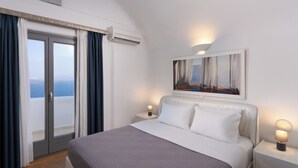Ein Hotelzimmer mit einem Bett, einem Nachttisch mit Lampe, einem Bild an der Wand und Meerblick durch eine Schiebetür.