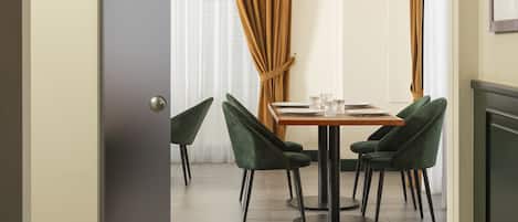 A hotel room with a dining area featuring a Martini sign, green chairs, and a table set for two.