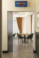 Habitación de hotel con comedor que incluye un cartel de Martini, sillas verdes y una mesa dispuesta para dos personas.