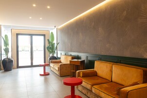 Un hall con un sofá, sillas, una mesa roja y plantas en macetas.