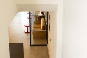 Un pasillo con una verja de metal negro, escaleras con alfombra color crema y taburetes circulares rojos.