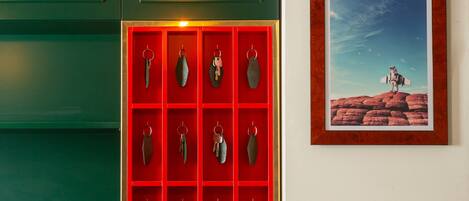 Zona de recepción con pared verde, expositor de llaves rojo, un cuadro enmarcado y una lámpara colgante.