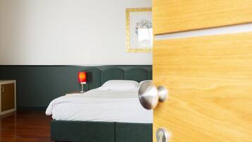 Une chambre à coucher avec un lit, une table de chevet avec une lampe, un tableau encadré au mur et une porte en bois.