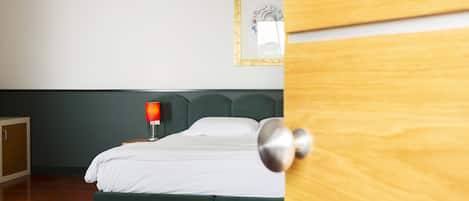 Quarto com cama, mesa de cabeceira com abajur, quadro na parede e porta de madeira.