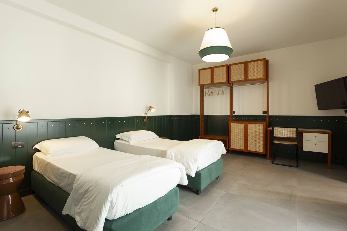 Habitación de hotel con dos camas, un escritorio, una silla, un armario y un televisor.