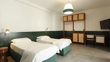 Habitación de hotel con dos camas, un escritorio, una silla, un armario y un televisor.