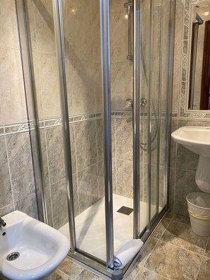 A bathroom with a glass-enclosed shower, a pedestal sink, and a marble-tiled wall. - Hostal Residencia Fornos (Santiago de Compostela)