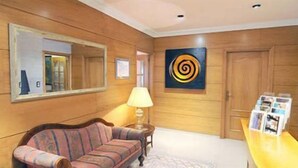 A room with wooden paneling, a sofa, a table with magazines, a lamp, and a painting. - Hostal Residencia Fornos (Santiago de Compostela)