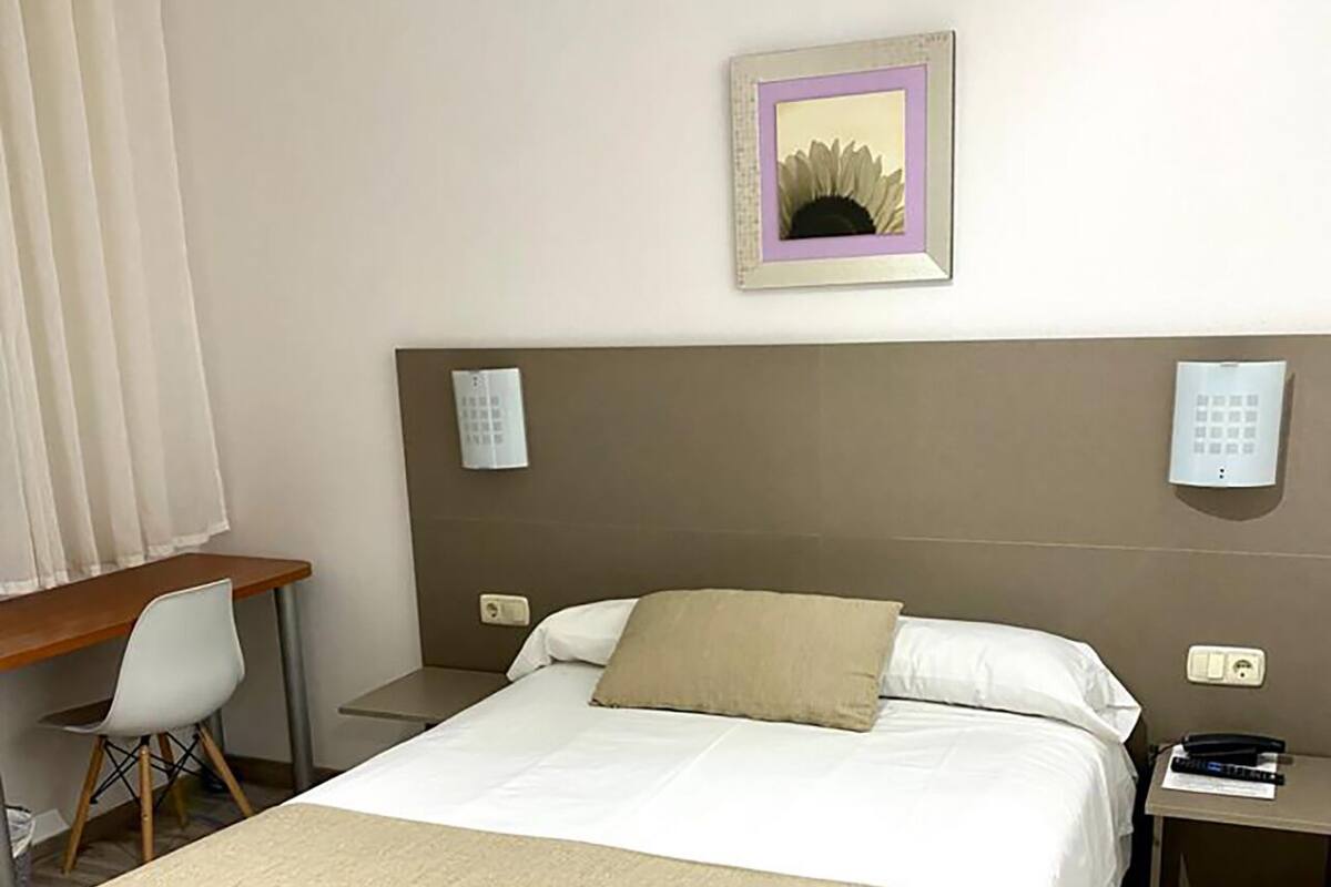 Una habitación de hotel con una cama grande, un escritorio, una silla y un teléfono instalado en la pared.