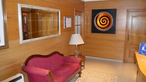 A hotel lobby with a wooden wall, a red patterned sofa, a lamp, a mirror, and a wall art piece. - Hostal Residencia Fornos (Santiago de Compostela)