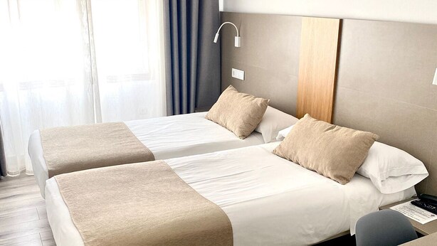 A hotel room with two beds, a wooden headboard, a bedside table, and a window with curtains. - Hostal Residencia Fornos (Santiago de Compostela)