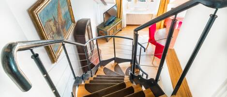 Una escalera de madera con barandillas negras, una silla roja y un cuadro en la pared.
