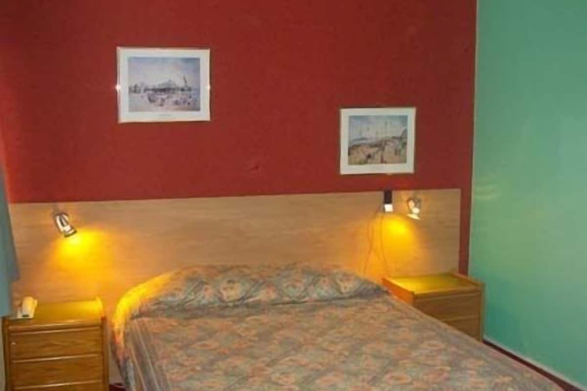 Une chambre à coucher comprenant un lit, deux tables de chevet et deux lampes fixées au mur.