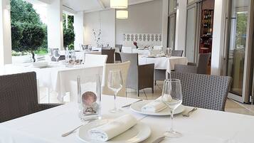 Un restaurante con manteles blancos, sillas de mimbre y una vitrina de vidrio para vinos.
