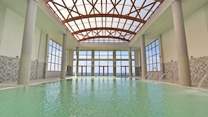 Ein Hallenbad mit hoher Decke und großen Fenstern.