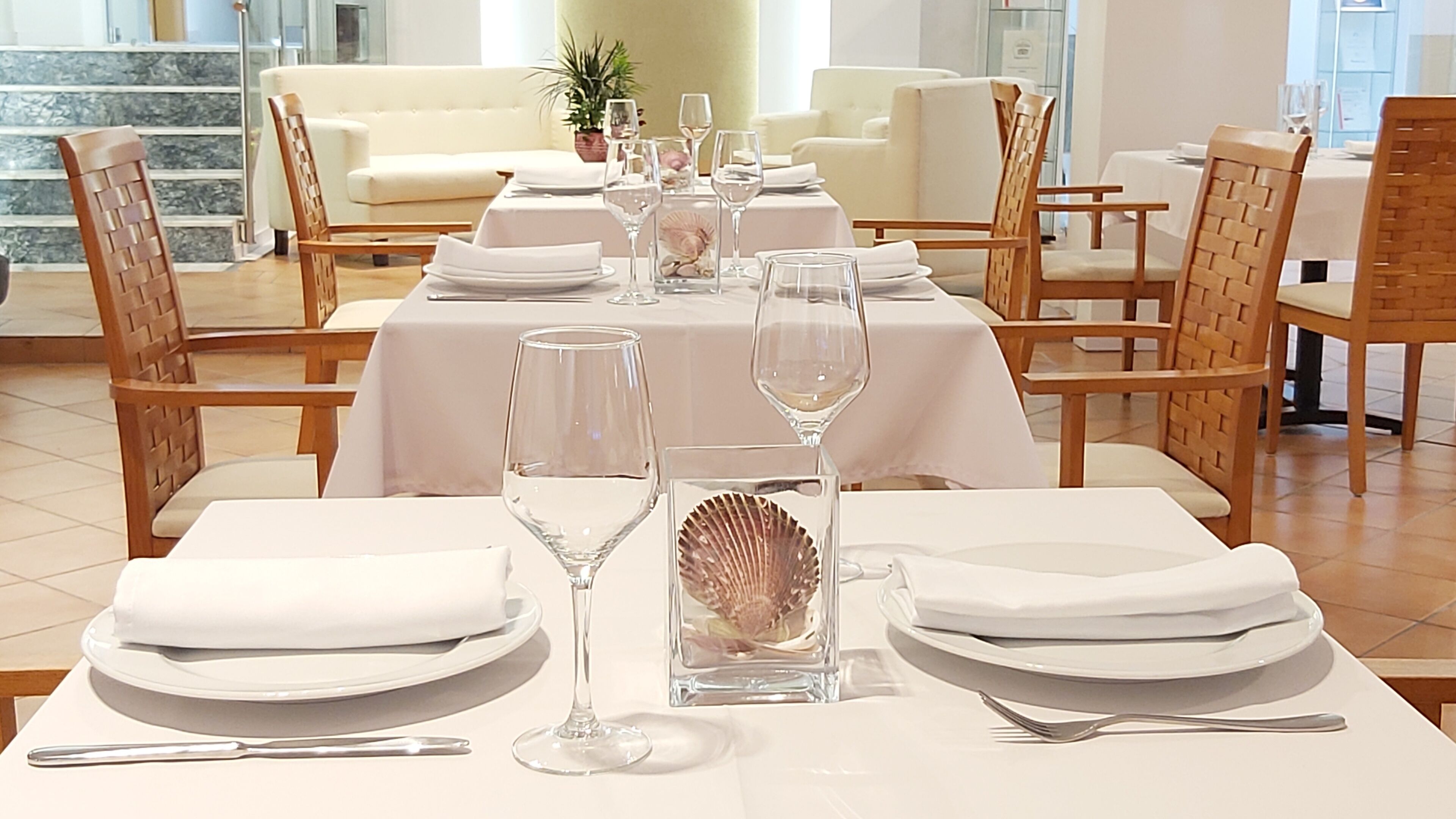 A dining area with white tablecloths, neatly set tables, and wicker chairs.