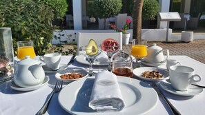 Un desayuno con gran variedad de alimentos y bebidas, que incluye un vaso de zumo de naranja, un cuenco de semillas de granada y un plato de almendras.
