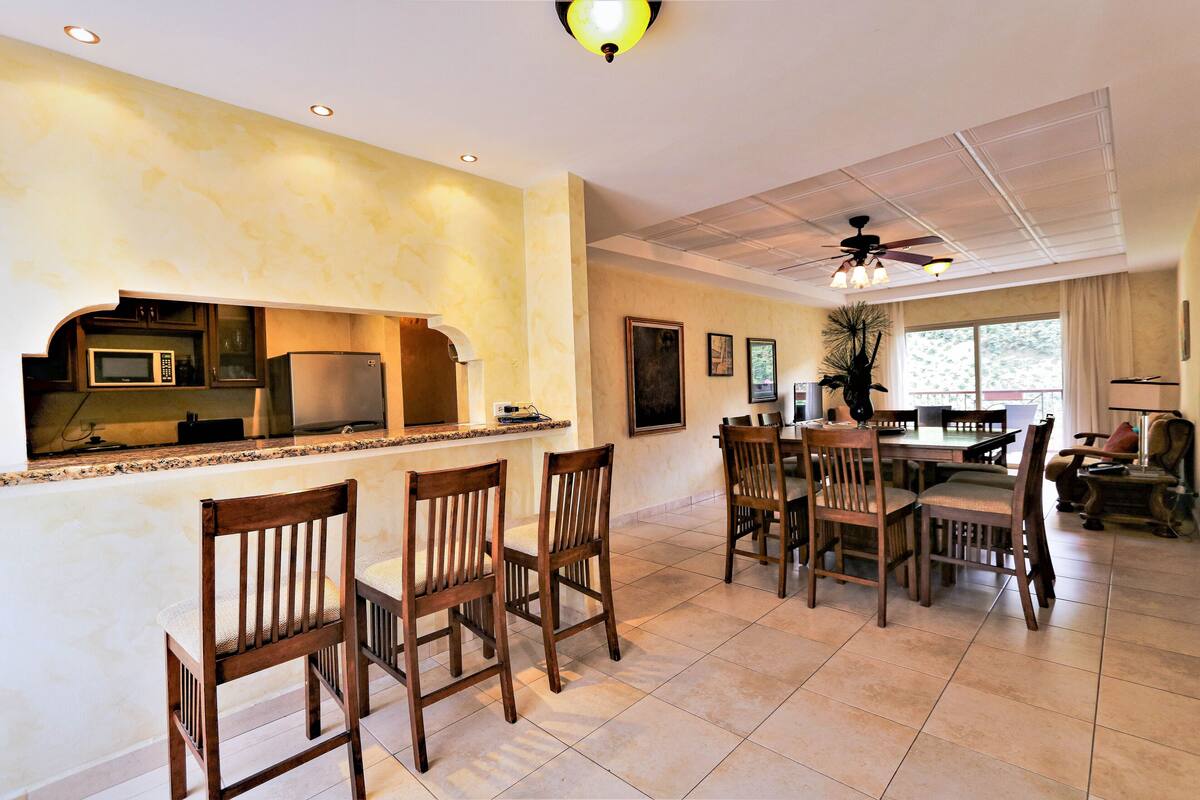A spacious kitchen with a dining area, featuring a microwave, refrigerator, and a large window.