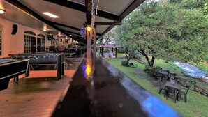 An outdoor patio area with a pool table, seating, and a view of a natural landscape including a stream and trees. - Hotel Valle del Rio, SA (Boquete)