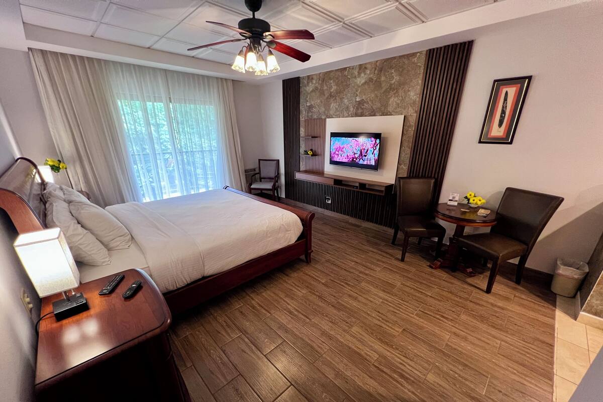 A hotel room with a bed, a desk, a chair, a TV, and a ceiling fan.