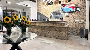 A hotel reception desk with a stone wall backdrop, a large mirror, and a vase of sunflowers. - Hotel Valle del Rio, SA (Boquete)