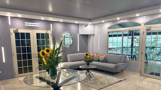 A modern living room with a glass coffee table, a grey sofa, and a large window with a balcony view. - Hotel Valle del Rio, SA (Boquete)