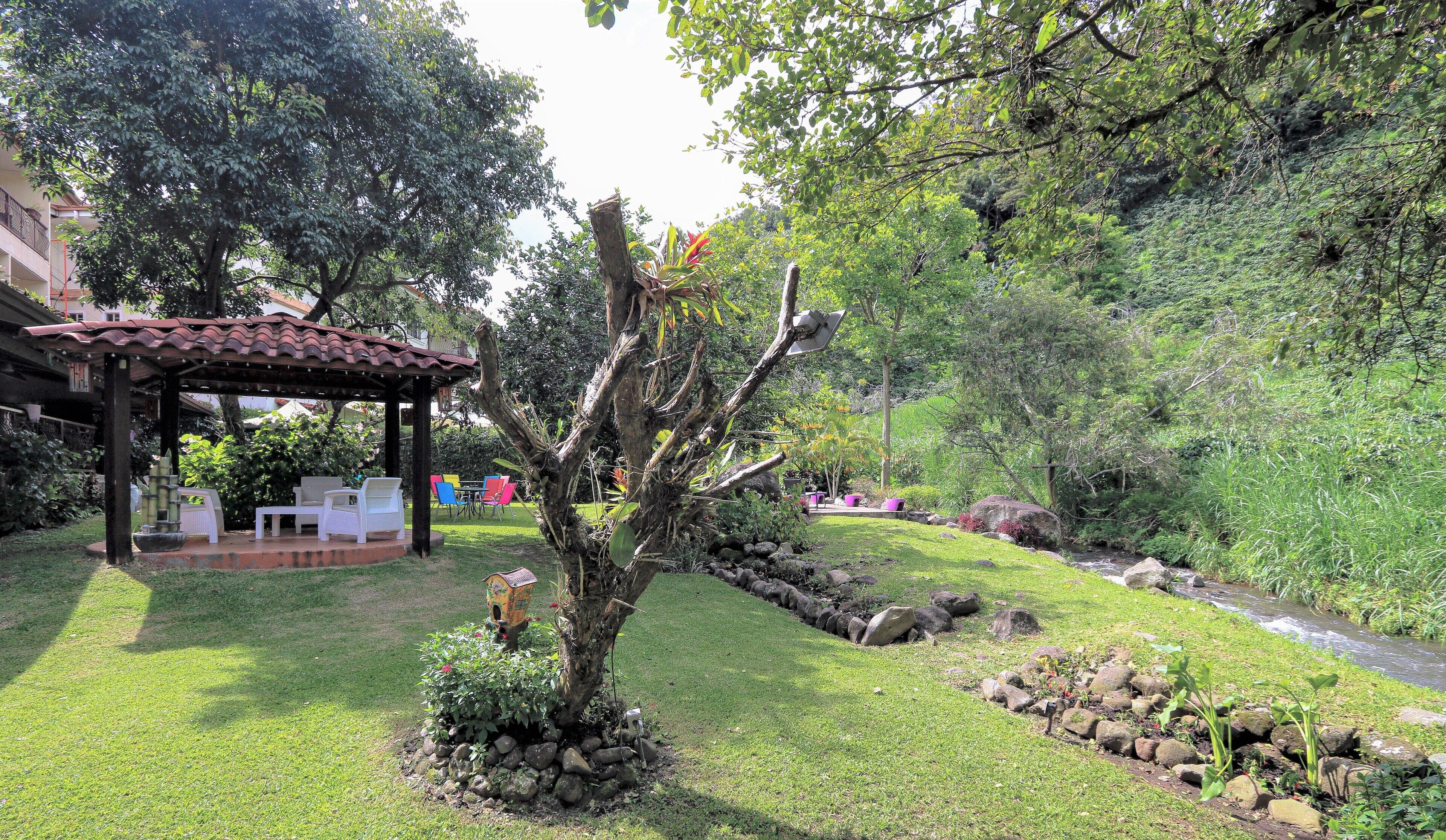 Un jardín con un pabellón, un arroyo pequeño y una gran variedad de plantas.