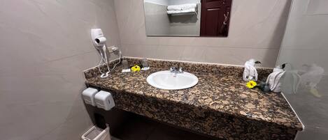 A bathroom with a granite countertop, a white sink, a mirror, a towel rack, and a trash bin.
